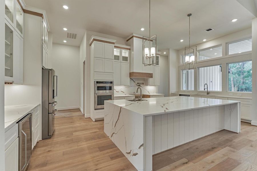 Designer kitchen featuring a striking waterfall island, sleek quartz surfaces, custom cabinetry, and abundant natural light for a bright, modern culinary space.