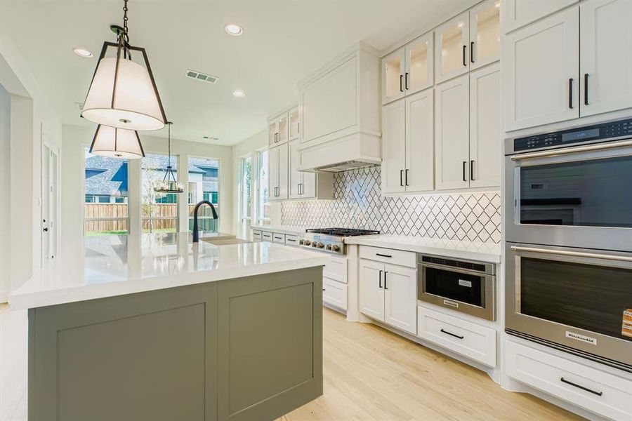 Kitchen featuring stainless steel appliances, white cabinetry, backsplash, decorative light fixtures, and glass insert cabinets Kitchen featuring stainless steel appliances, white cabinetry, backsplash, decorative light fixtures, and glass insert cabinets