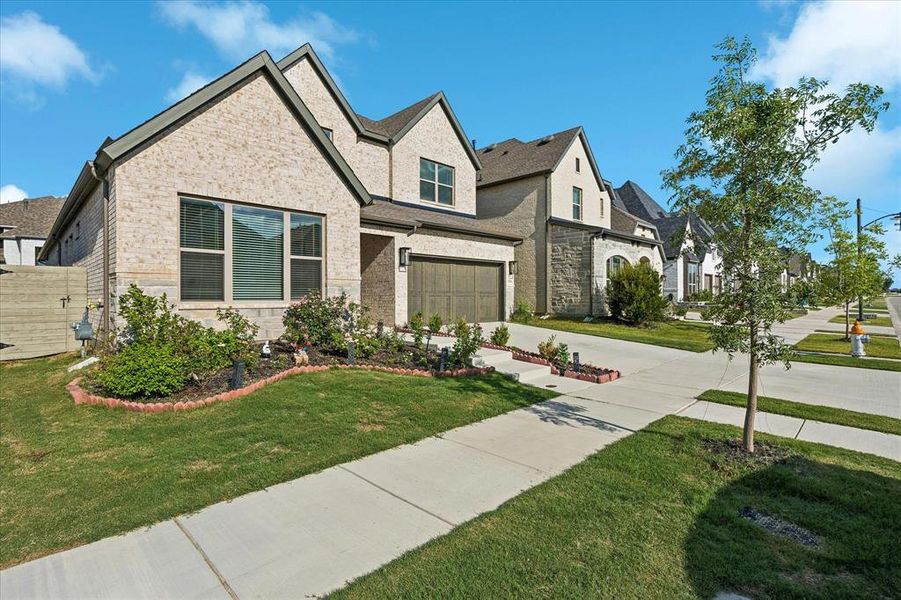 Contemporary exterior featuring light brick, dark trim, an attached garage with a wood-finish door, a manicured lawn, and mature landscaping Contemporary exterior featuring light brick, dark trim, an attached garage with a wood-finish door, a manicured lawn, and mature landscaping