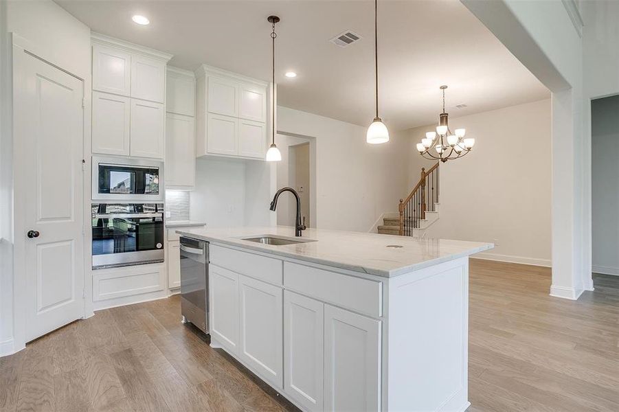 Kitchen with a kitchen island with sink, stainless steel appliances, white cabinets, and light hardwood / wood-style floors