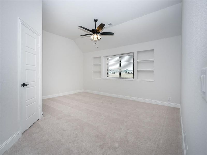 Spare room featuring light carpet, lofted ceiling, built in shelves, and ceiling fan Spare room featuring light carpet, lofted ceiling, built in shelves, and ceiling fan