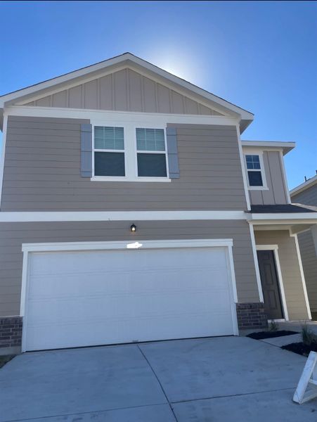 View of front facade with board and batten siding, driveway, an attached garage, and stone siding