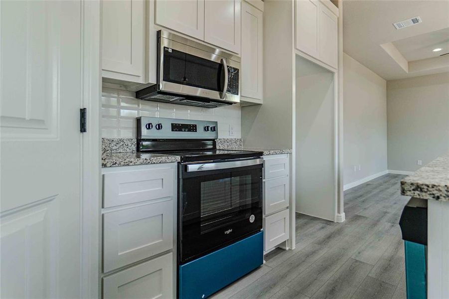 Kitchen featuring white cabinetry, light stone countertops, a raised ceiling, light hardwood / wood-style floors, and appliances with stainless steel finishes