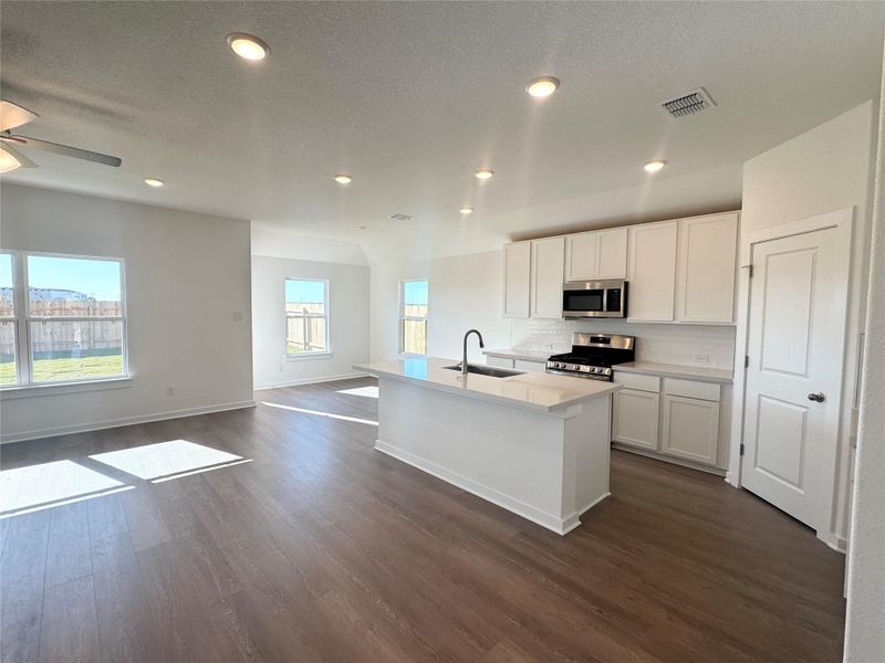 Kitchen with an island with sink, a textured ceiling, stainless steel appliances, decorative backsplash, and white cabinetry