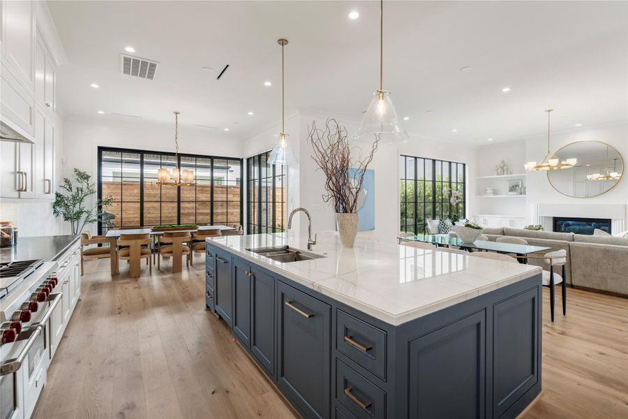 A look at the kitchen and living room. The dark steel windows add pizzazz to the aesthetic and pair well with the island. A deep chef’s sink with Ruvati Workstation is great for food prep, and the polished nickel fixtures gleam in the light. Kate Cone pendants and recessed cans illuminate the space.