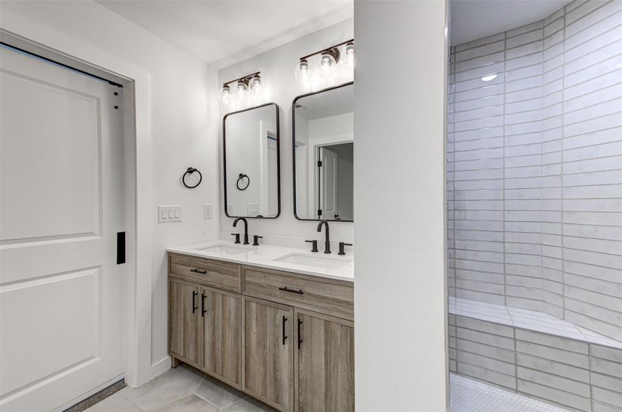Bathroom with light tile patterned flooring, double vanity, and a tile shower
