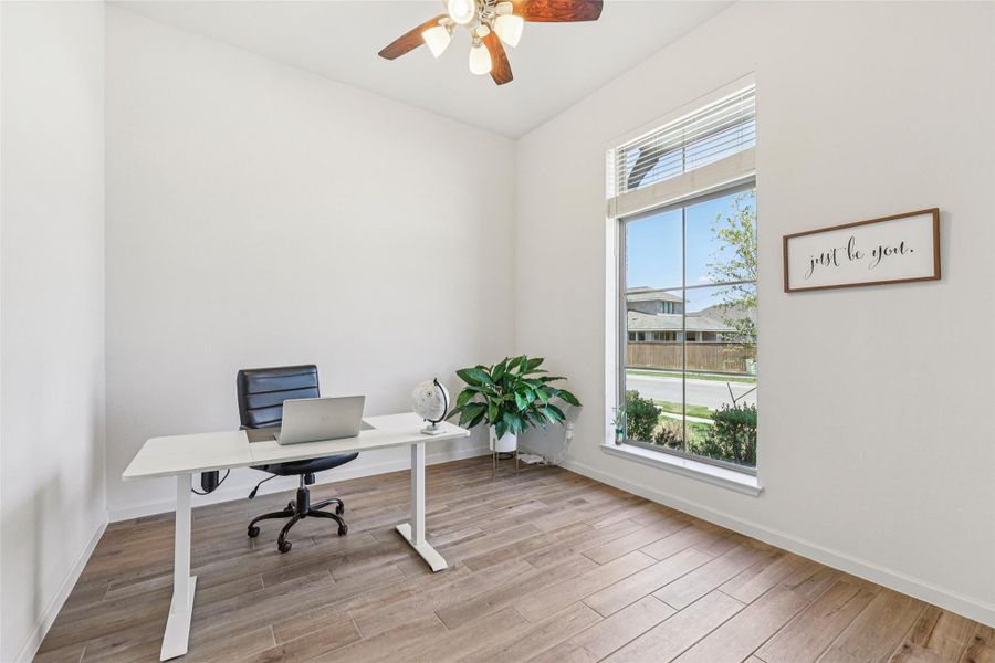 This room features a ceiling fan with light fixture, large windows providing natural light, and wood-look tile flooring