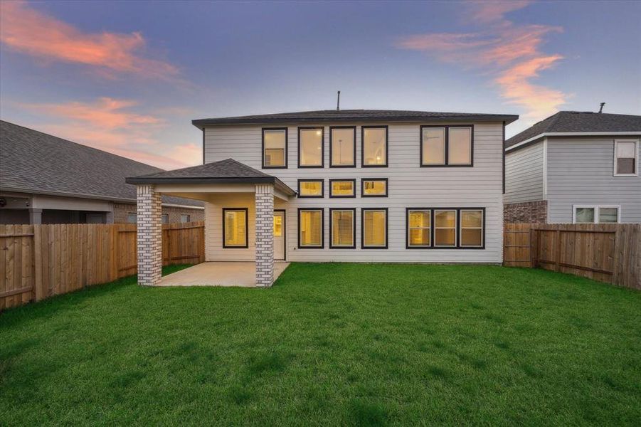 The spacious backyard features a covered patio, perfect for outdoor dining or relaxation. Large windows across the back of the home flood the living spaces with natural light, creating an open, airy atmosphere that connects the indoor and outdoor living areas.