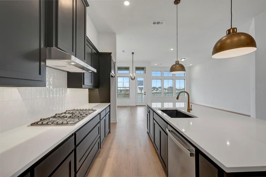 Kitchen with a spacious island, light wood finished floors, stainless steel appliances, pendant lighting, and decorative backsplash