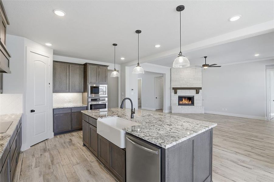 Kitchen with appliances with stainless steel finishes, a kitchen island with sink, decorative light fixtures, a large fireplace, and light wood finished floors
