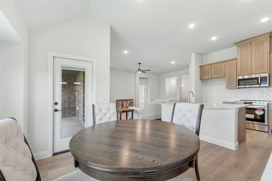 Open-concept dining area with round wood table leading to kitchen with light wood cabinets and stainless steel appliances