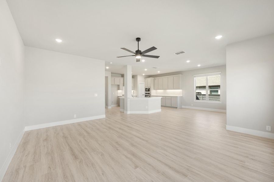 Open living area with light wood floors, ceiling fan, and kitchen with island and gray cabinets in background