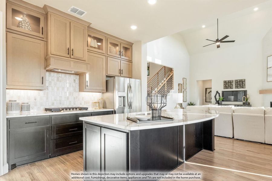 Open kitchen with curved dark island, tan cabinets, white countertops, and hardwood floors opening to living room Open kitchen with curved dark island, tan cabinets, white countertops, and hardwood floors opening to living room
