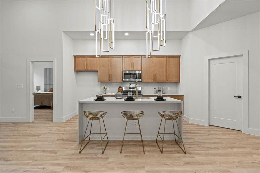 Kitchen featuring appliances with stainless steel finishes, a high ceiling, baseboards, and light wood-style flooring Kitchen featuring appliances with stainless steel finishes, a high ceiling, baseboards, and light wood-style flooring