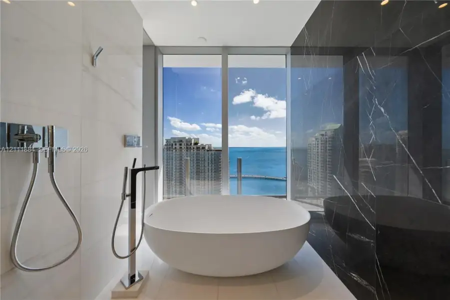 Freestanding soaking tub, floor-to-ceiling windows, high-contrast wall tiling, polished chrome fixtures, and open water scenery Freestanding soaking tub, floor-to-ceiling windows, high-contrast wall tiling, polished chrome fixtures, and open water scenery