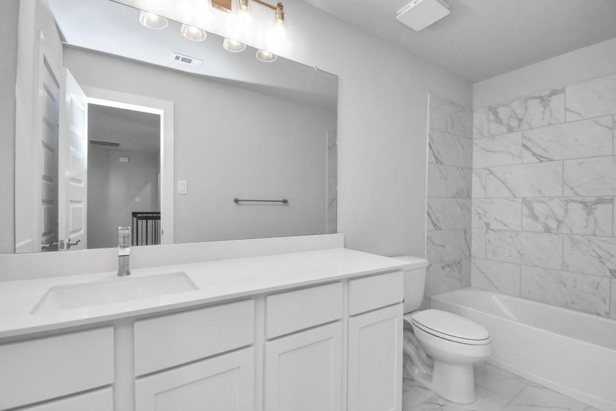 Secondary bath features tile flooring, bath/shower combo with tile surround, light stained wood cabinets, beautiful light countertop.
