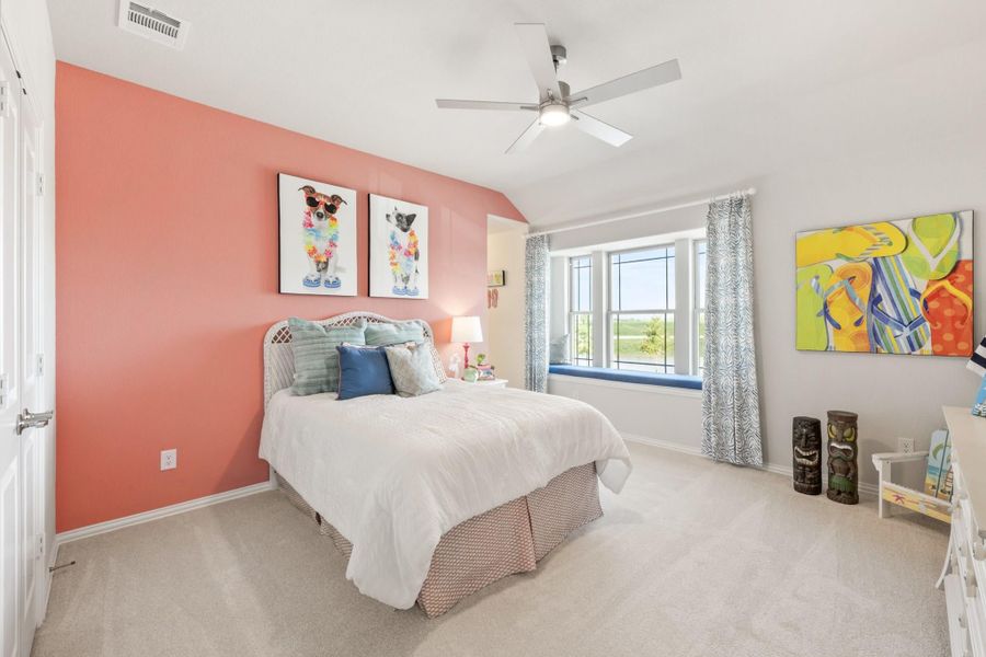 Bedroom with coral accent wall, ceiling fan, carpet flooring, and window seat with natural light Bedroom with coral accent wall, ceiling fan, carpet flooring, and window seat with natural light