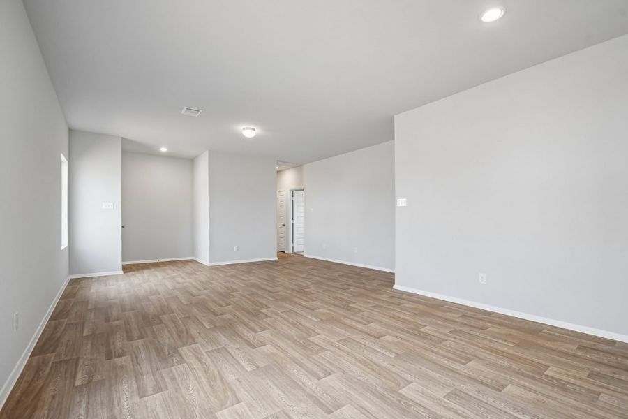 Image of home living room looking towards the front door on the left and hallway to bedrooms on the right. Wood-look flooring, white walls and doors, and a window on the left