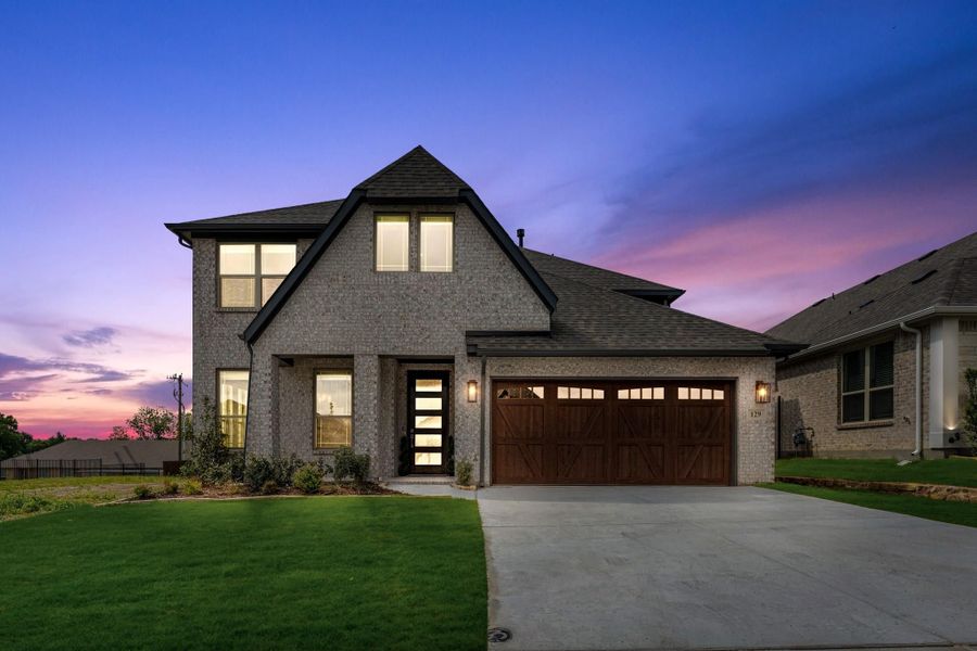 Two-story brick home with dark roof, two-car garage, and concrete driveway at dusk