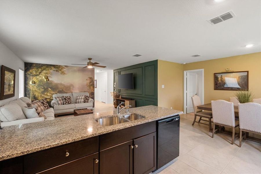 Kitchen with dark brown cabinets, light stone countertops, dishwasher, open floor plan, and light tile patterned floors