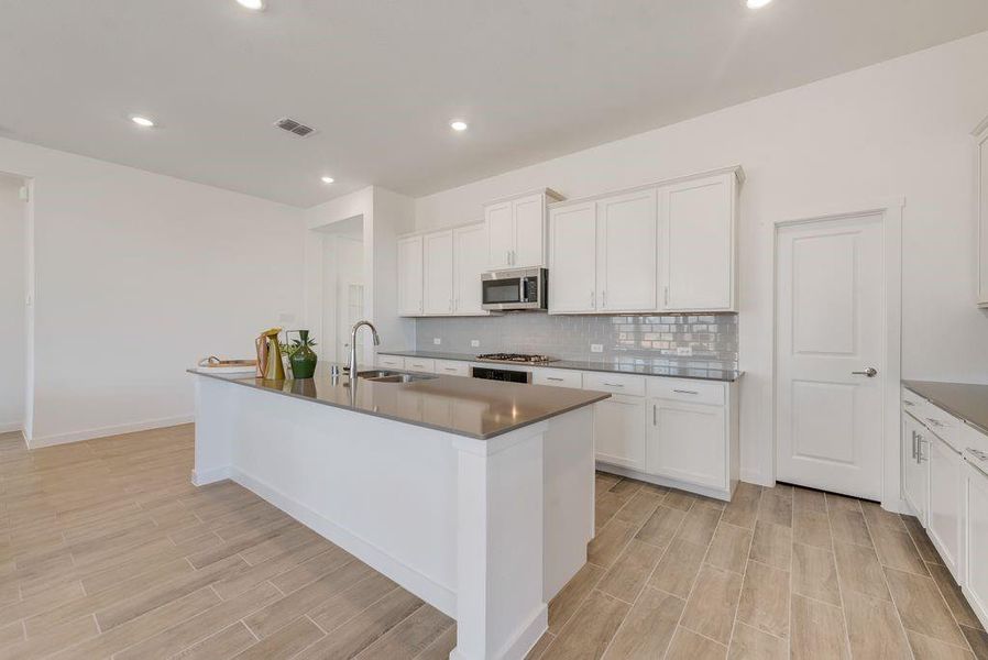 Kitchen with appliances with stainless steel finishes, light wood-style flooring, backsplash, a center island with sink, and white cabinetry