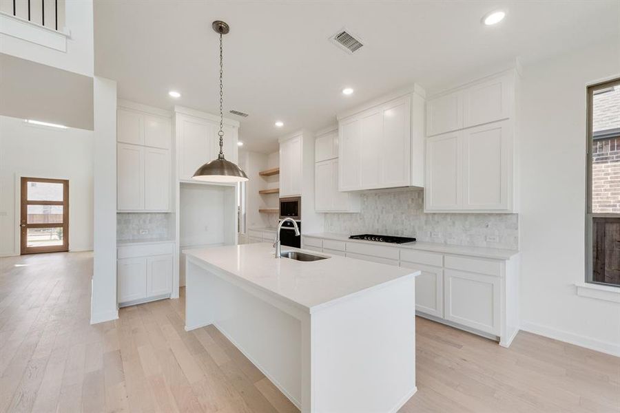 Kitchen with open shelves, decorative light fixtures, light wood-style flooring, white cabinetry, and an island with sink Kitchen with open shelves, decorative light fixtures, light wood-style flooring, white cabinetry, and an island with sink