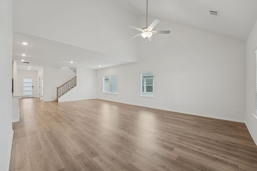 Unfurnished living room with light wood-type flooring, stairs, ceiling fan, and high vaulted ceiling