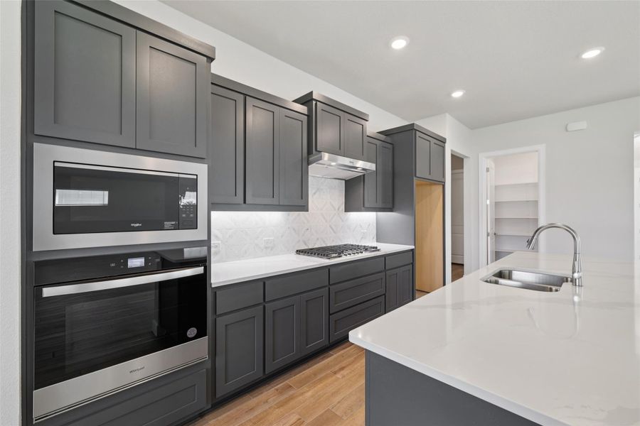 Kitchen featuring stainless steel appliances, light wood-style flooring, decorative backsplash, recessed lighting, and under cabinet range hood
