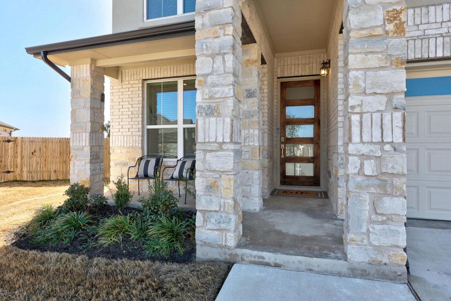 Property entrance with stone siding, brick siding, fence, and covered porch