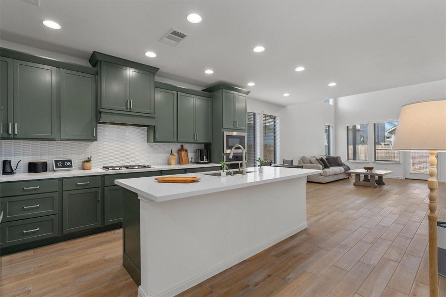 Kitchen featuring green cabinets, open floor plan, light wood-style flooring, and recessed lighting