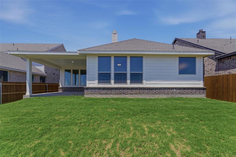 Expansive green lawn backing to a residential structure featuring a covered patio, multiple windows, and a brick foundation Expansive green lawn backing to a residential structure featuring a covered patio, multiple windows, and a brick foundation