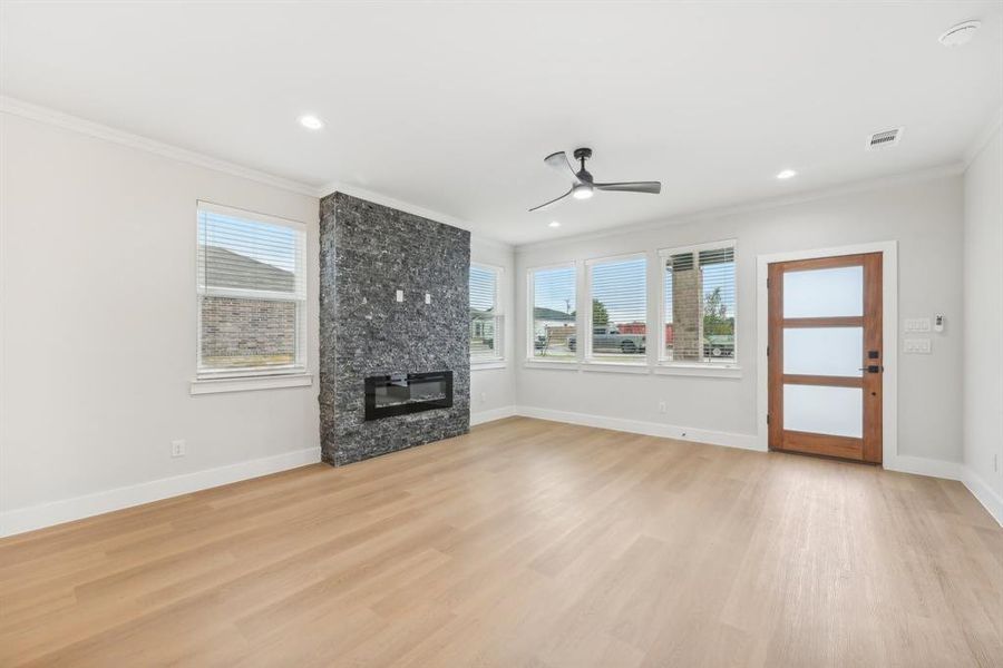 Unfurnished living room with light wood-type flooring, ceiling fan, a fireplace, and crown molding