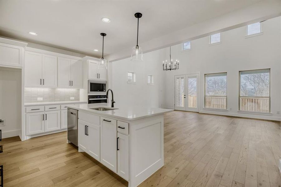 Kitchen featuring light wood-style floors, white cabinetry, a kitchen island with sink, decorative backsplash, and wall oven