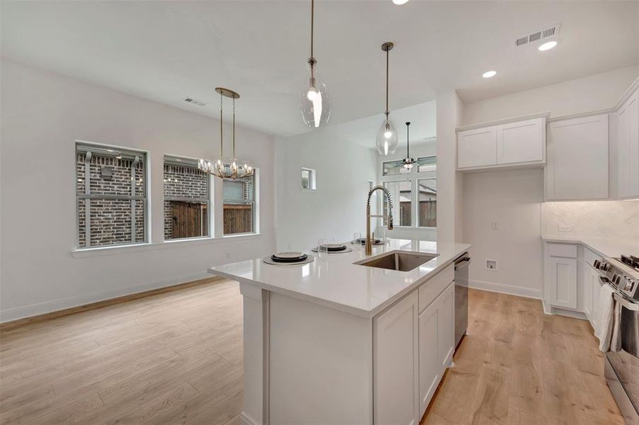 Open-concept kitchen and dining area featuring a central island with an undermount sink, quartz countertops, white cabinetry, and wood-finish flooring