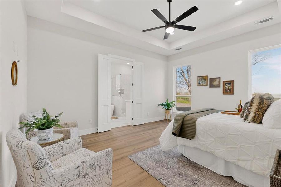 Bedroom with light wood-type flooring, a tray ceiling, ensuite bathroom, ceiling fan, and recessed lighting