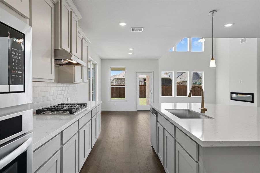 Kitchen featuring stainless steel appliances, dark wood-type flooring, tasteful backsplash, decorative light fixtures, and light stone countertops Kitchen featuring stainless steel appliances, dark wood-type flooring, tasteful backsplash, decorative light fixtures, and light stone countertops