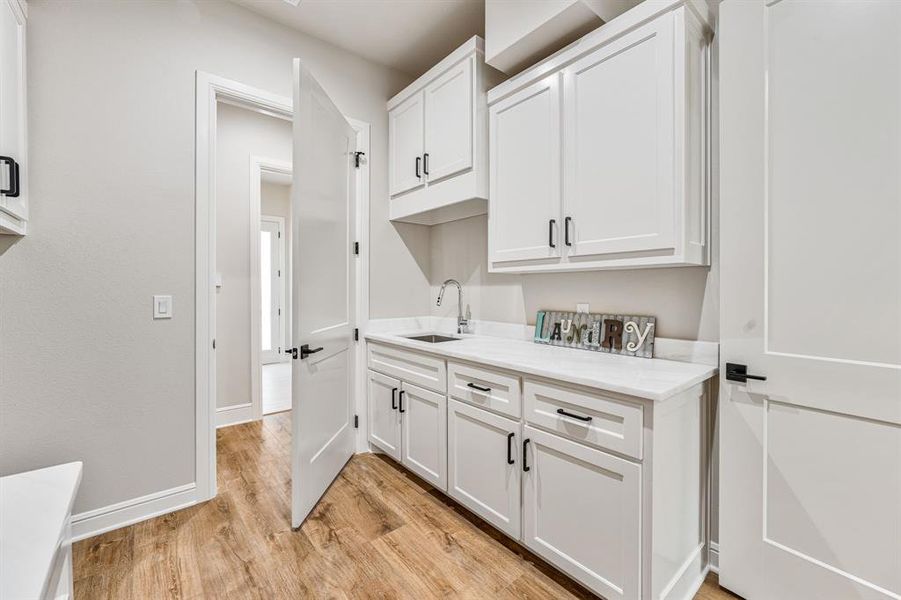 Clothes washing area featuring sink and light hardwood / wood-style flooring