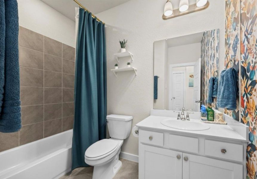 This well-appointed guest bathroom offers a modern aesthetic with its clean white vanity, tiled tub/shower combo, and fun pops of color!