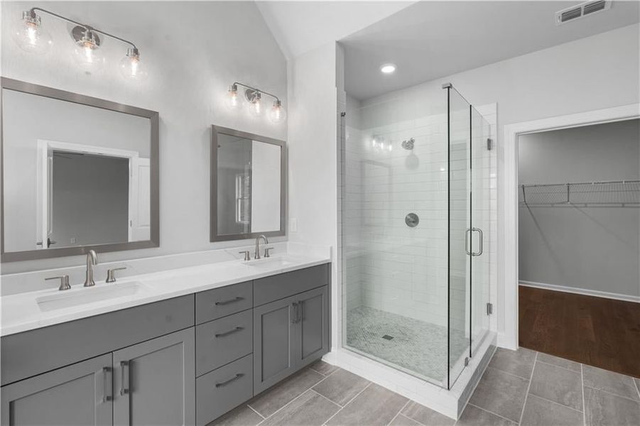 Bathroom with a shower stall, double vanity, a walk in closet, vaulted ceiling, and recessed lighting Bathroom with a shower stall, double vanity, a walk in closet, vaulted ceiling, and recessed lighting