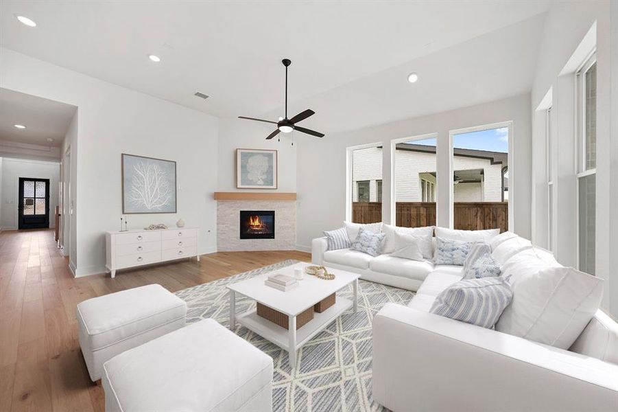 Living room featuring recessed lighting, wood finished floors, a warm lit fireplace, and a ceiling fan Living room featuring recessed lighting, wood finished floors, a warm lit fireplace, and a ceiling fan