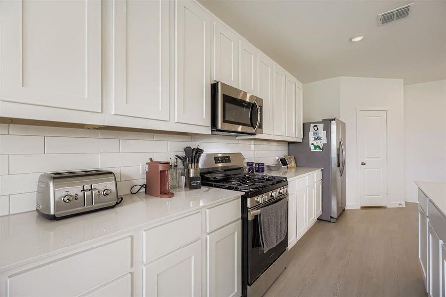 Kitchen featuring appliances with stainless steel finishes, white cabinets, tasteful backsplash, light wood-type flooring, and recessed lighting