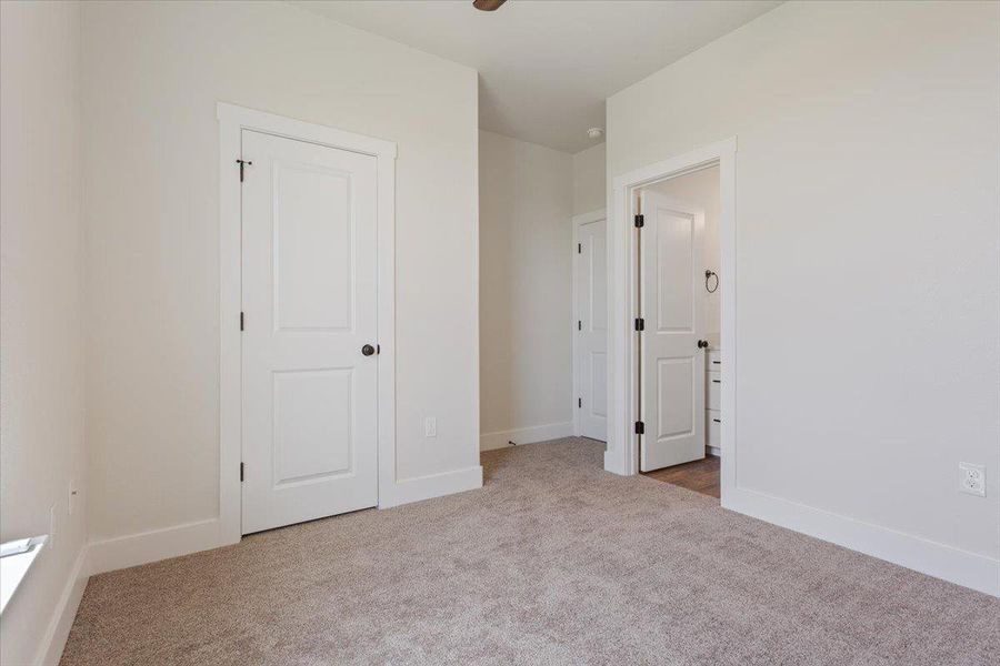 A well-lit bedroom features plush carpeting and white trim, leading to a connected private bath.