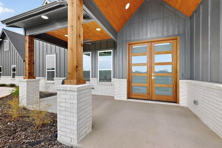 Entrance to property with board and batten siding, brick siding, and covered porch