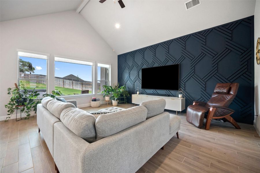 Living area with an accent wall, high vaulted ceiling, a ceiling fan, wood finished floors, and beam ceiling