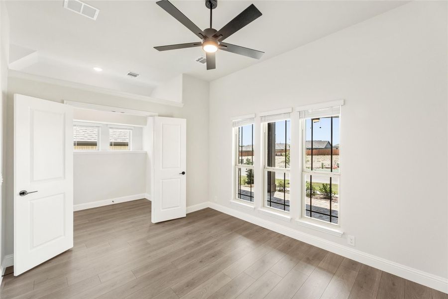 Empty bedroom with hardwood floors, ceiling fan, large windows, and open door to closet or hallway Empty bedroom with hardwood floors, ceiling fan, large windows, and open door to closet or hallway