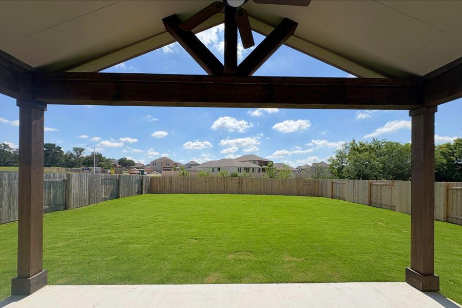 Expansive backyard featuring a manicured lawn, full privacy fencing, and a covered patio with exposed wood beams and a ceiling fan