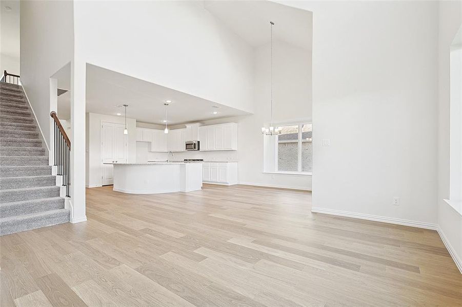 Unfurnished living room with a notable chandelier, a high ceiling, and light wood-type flooring