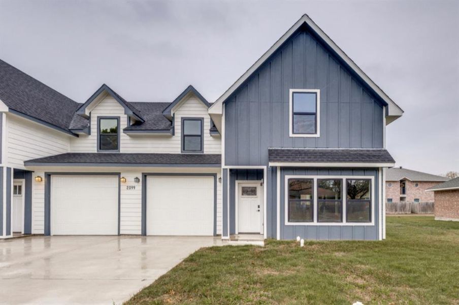 View of front of property with board and batten siding, a garage, roof with shingles, driveway, and a front lawn