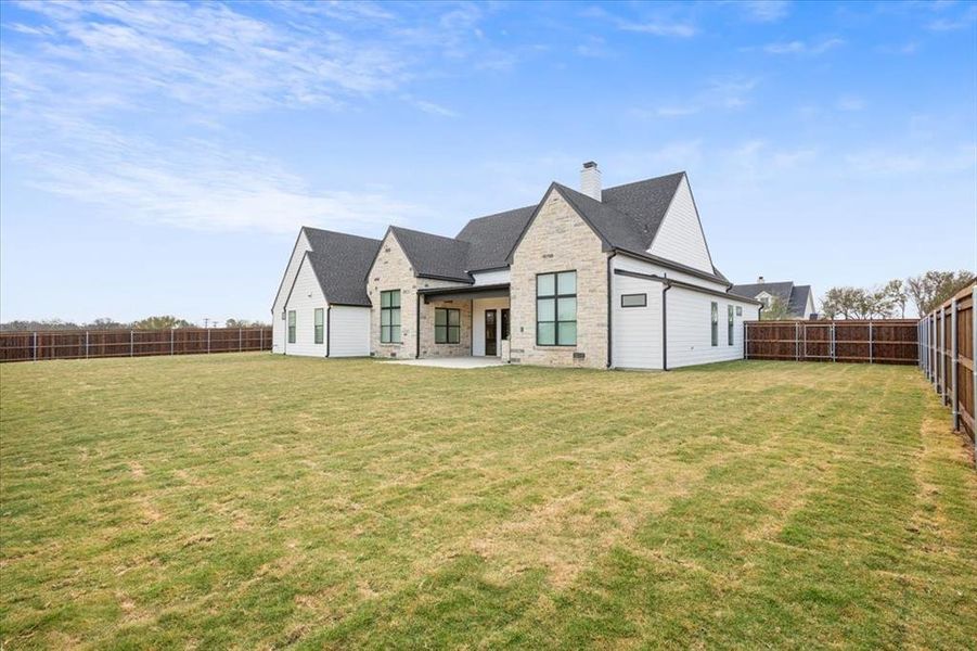 Back of property with a fenced backyard, a patio, a chimney, and stone siding