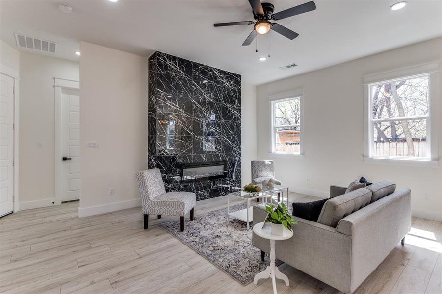 Living area featuring a premium fireplace, visible vents, wood finished floors, and a ceiling fan